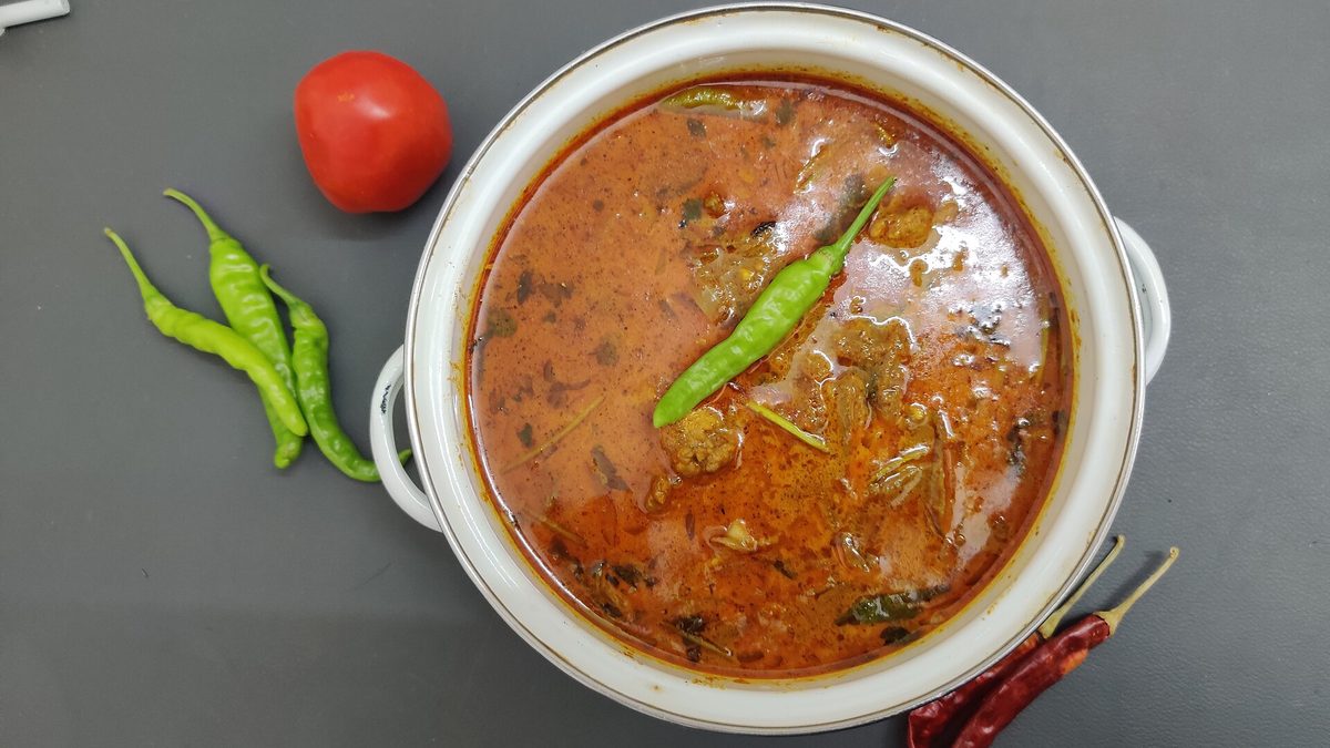 Steel ke bartan mein paki hui chicken curry, hari mirch aur tamatar ke saath